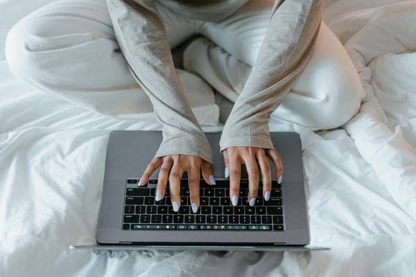 A person on their laptop sitting cross-legged on a comfortable bed